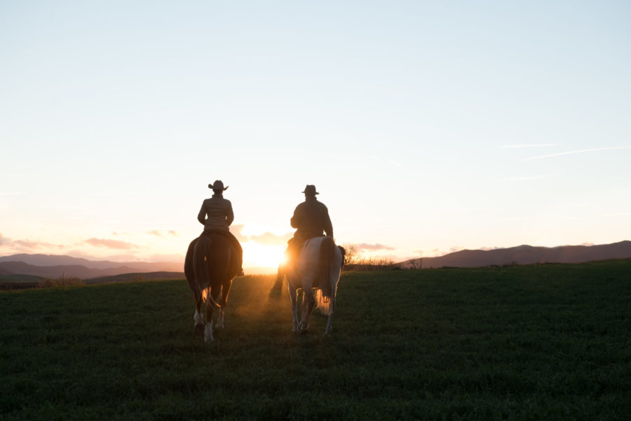The Freedom Point - Man and woman riding horses against sunset sky on ranch