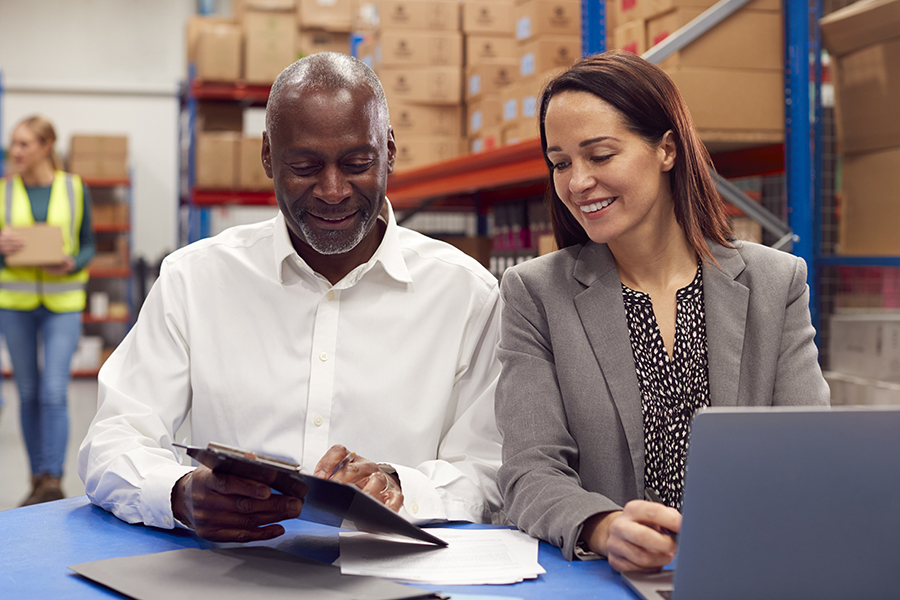 Distribution partners (a man and a woman) work in a warehouse on a laptop