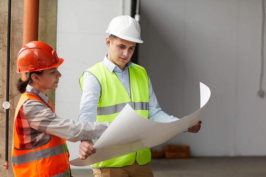 Two construction workers in work helmets examining the blueprint discussing business valuation